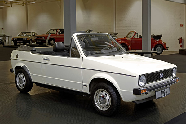 White VW Golf Cabriolet convertible in a garage with classic Golfs and Beetles