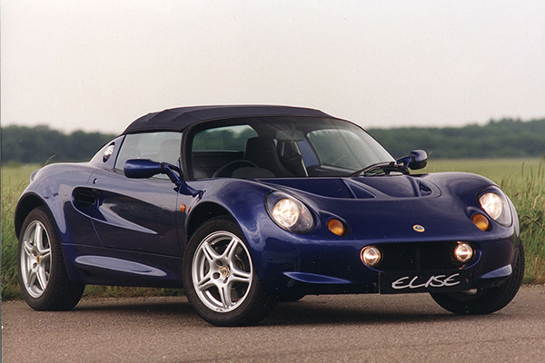 Dark Blue Lotus Elise With Grass Tree And Sky Backdrop