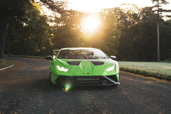 Verde mantis green mantis Lamborghini Huracan STO driving along a grass verge with trees in the background