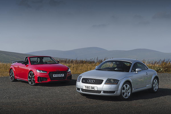 A Red And A Silver Audi TT With Green Mountainous Backdrop