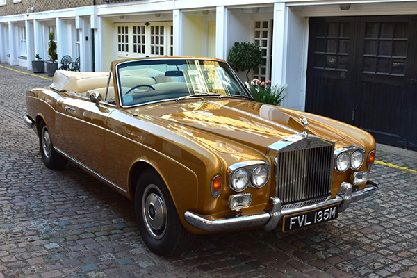 Gold Rolls Royce Corniche convertible beside mews on a cobbled road