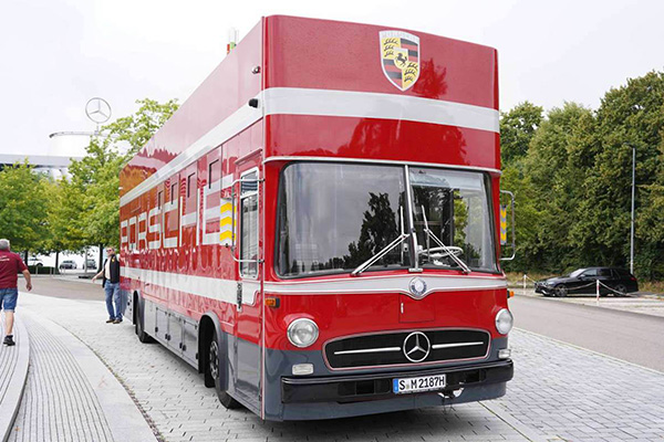 Red Mercedes Benz O317 Porsche logoed k r ace transporter On A Tree Lined Road Mercedes Building In The Background