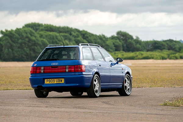 Back view of blue Audi RS2 Avant driving on track with fields and trees backdrop