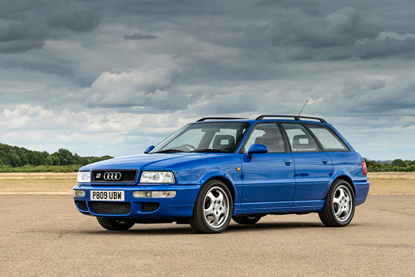 Front view of stationary blue Audi RS2 Avant with fields and trees backdrop