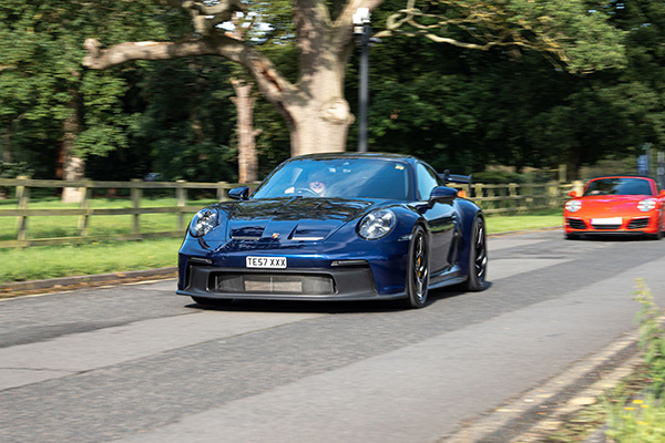 Dark blue Porsche 911 driving beside grass and trees